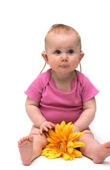 baby wearing hearing aid and holding a flower looking in the direction of the camera
